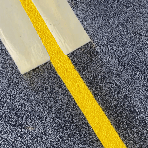 Ligne de marquage jaune fraîchement appliquée sur un sol en enrobé.