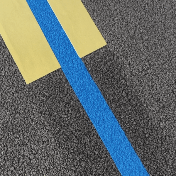 Ligne bleue de peinture de traçage appliquée sur sol asphalté.